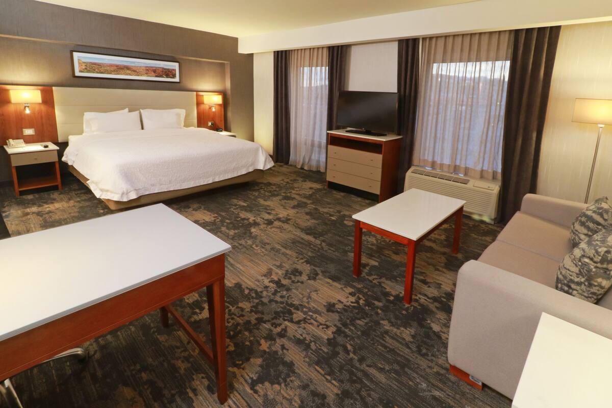 A hotel room with a bed, a desk, a sofa, a TV, and a window with curtains.