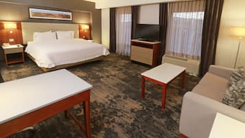 A hotel room with a bed, a desk, a sofa, a TV, and a window with curtains.