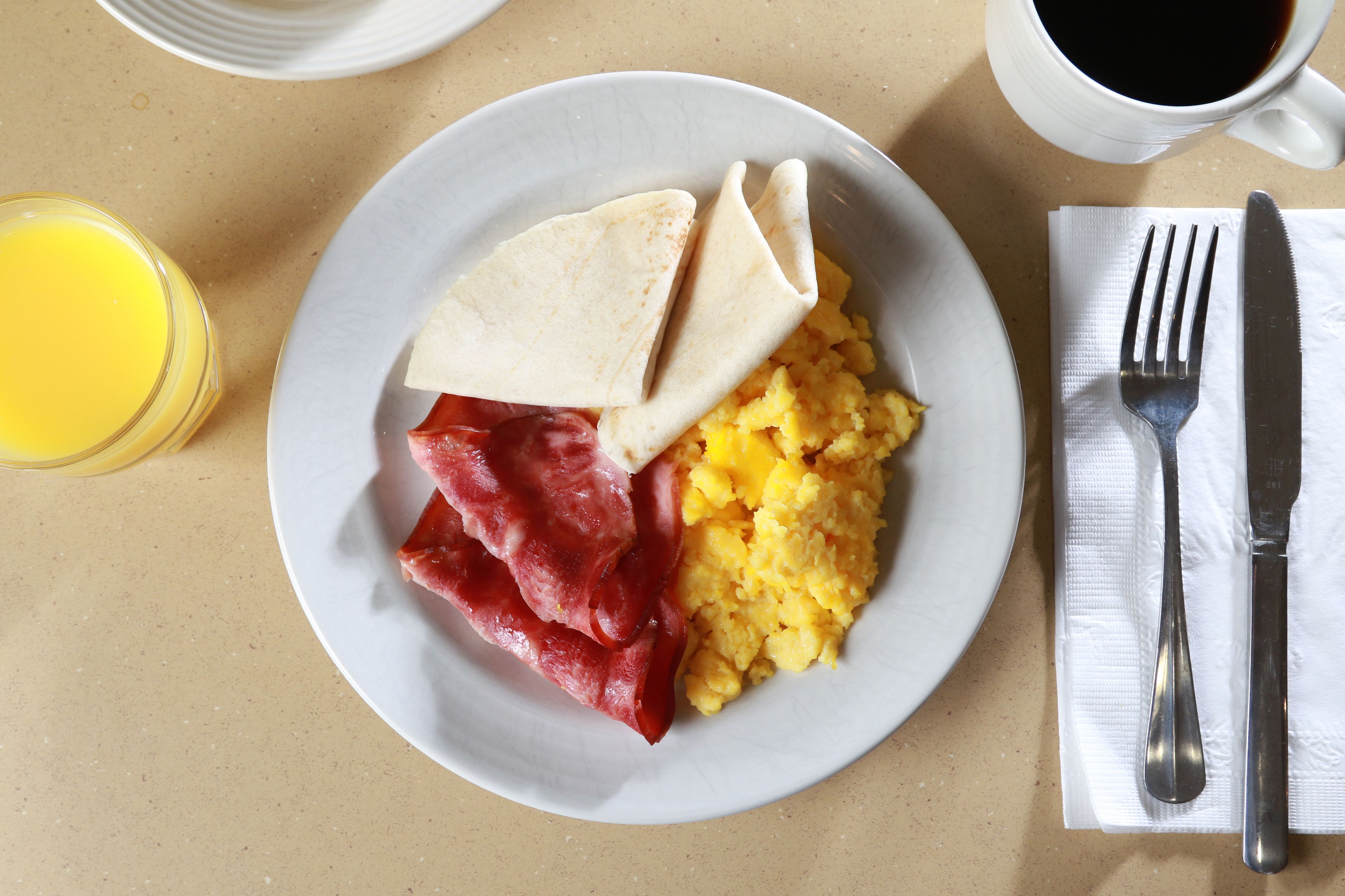 A plate with scrambled eggs, bacon, and a tortilla on a table.