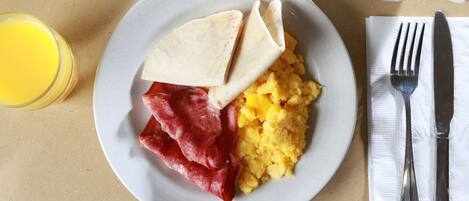Un plato con huevos revueltos, tocino y una tortilla sobre una mesa.