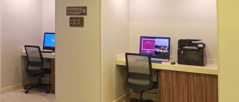 Zona de recepción de un hotel con dos escritorios, computadoras, sillas y una máquina de café.