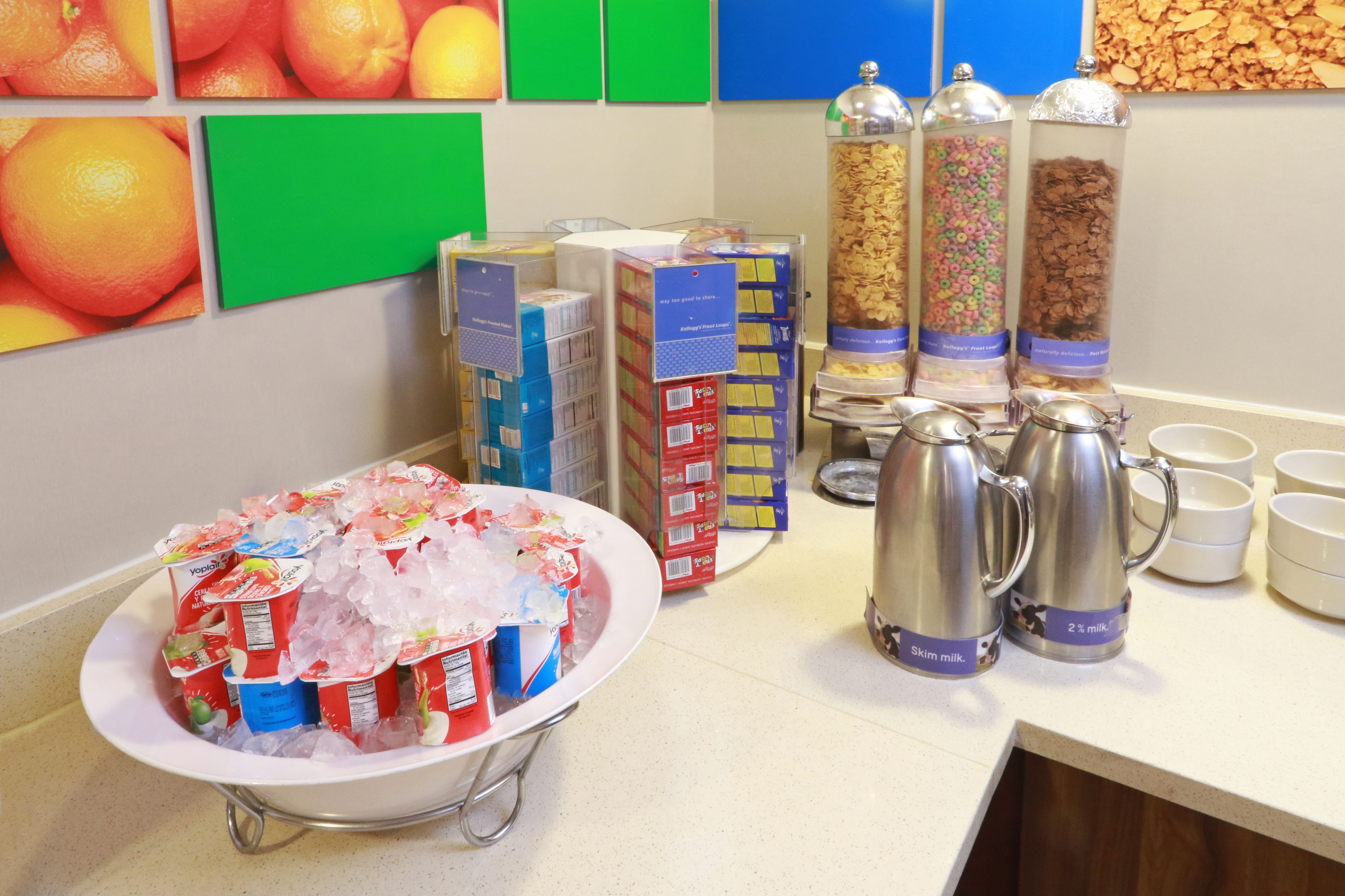 A breakfast buffet setup with yogurt cups, cereal bars, and coffee urns.