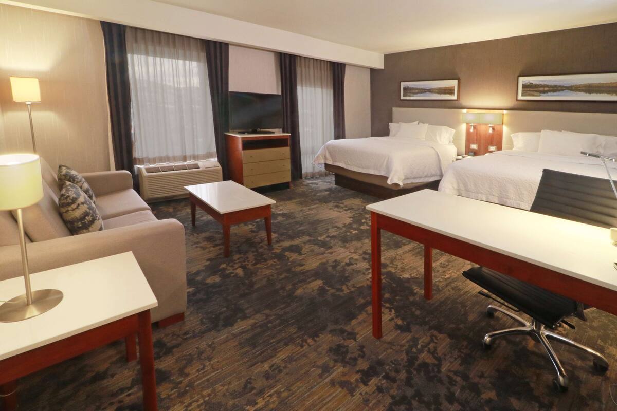 A hotel room with a bed, a desk, a chair, a sofa, and a TV.