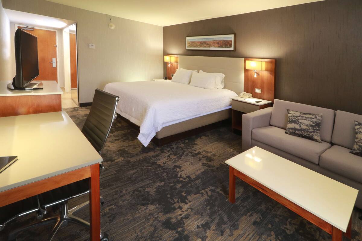 A hotel room with a bed, a sofa, a desk, and a TV.