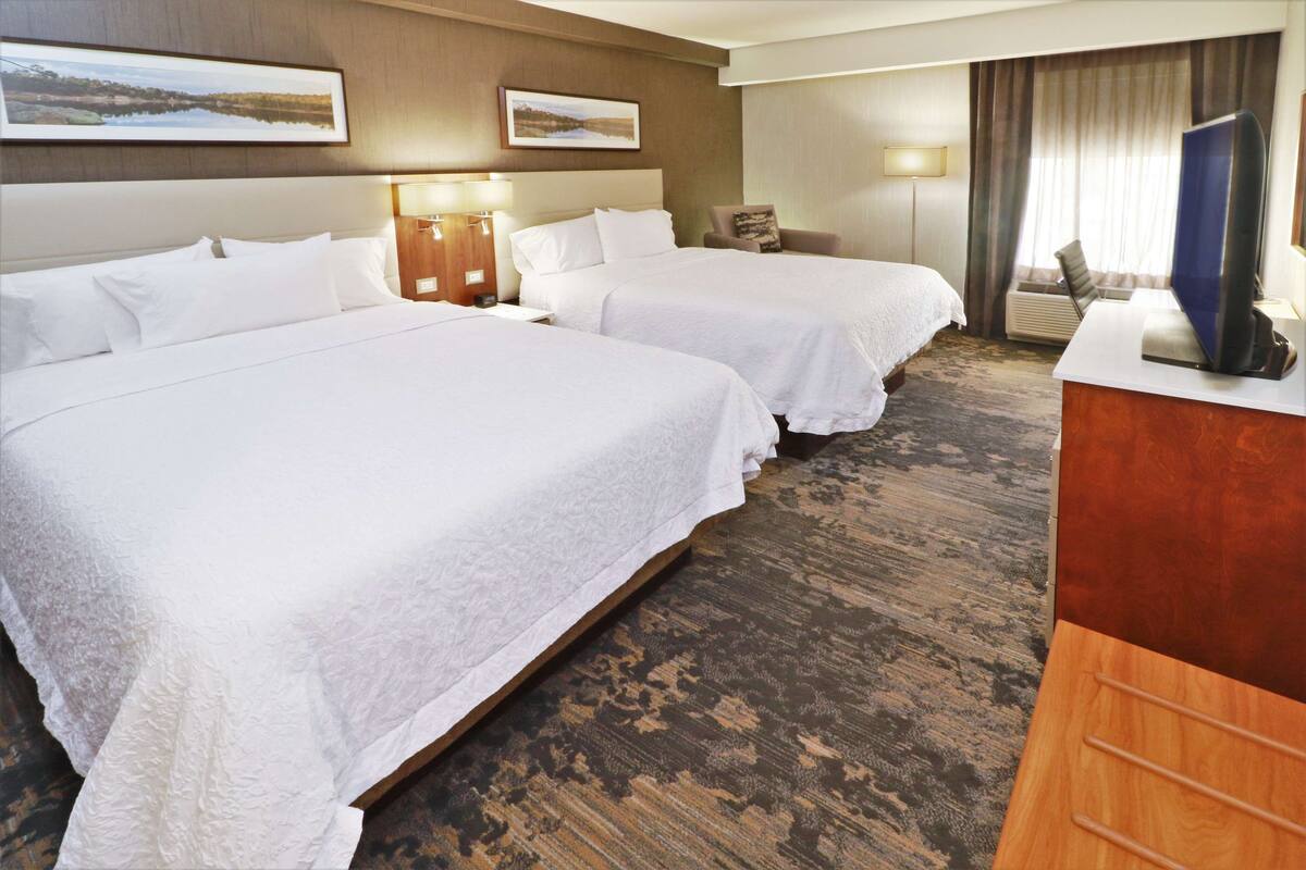 A hotel room with two beds, a desk, a chair, and a television.
