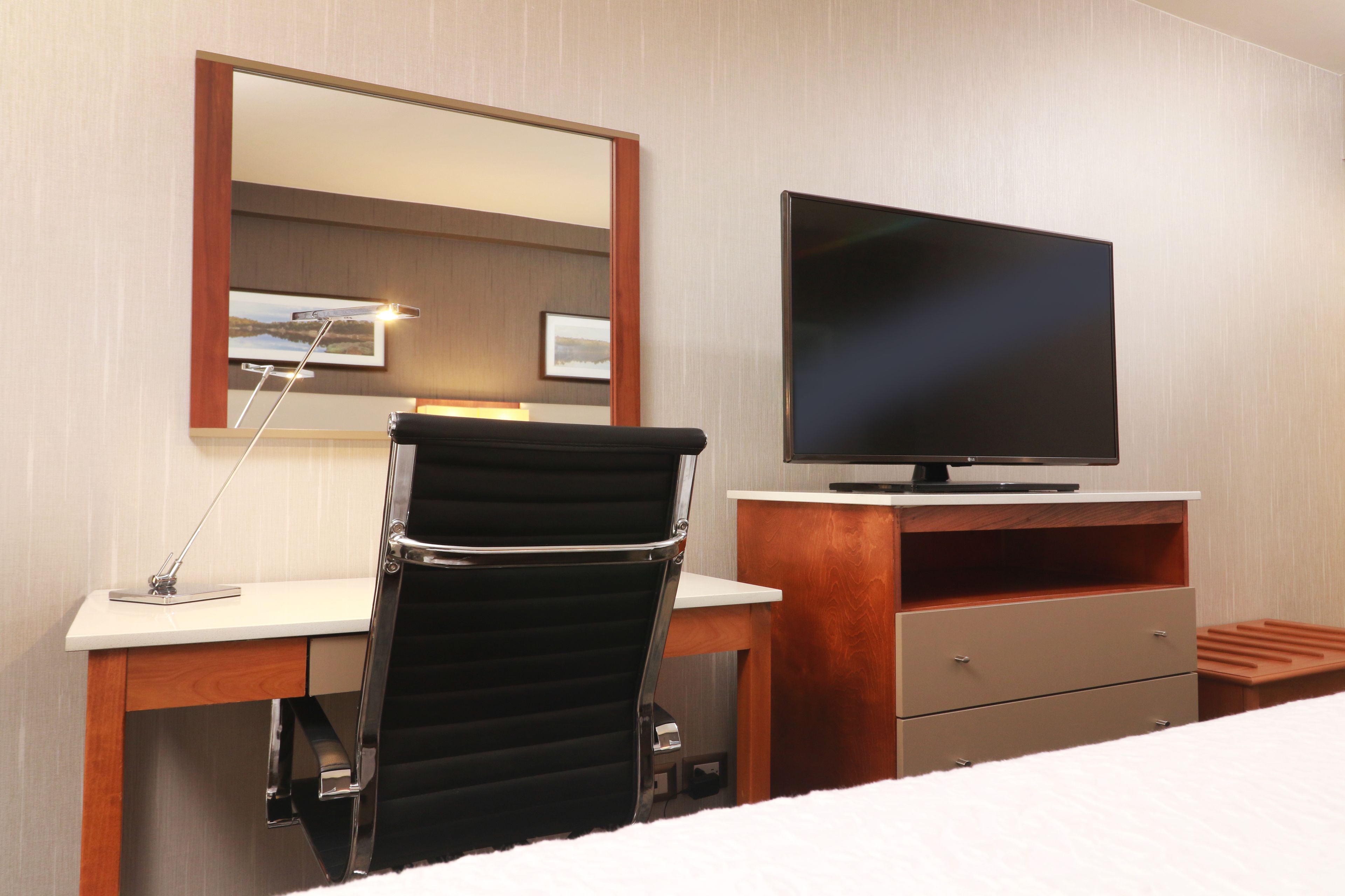 A hotel room with a bed, a desk with a chair, a television, and a mirror.