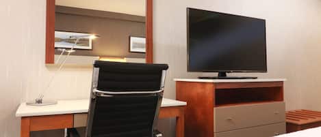 Una habitación de hotel con cama, escritorio, silla, televisor y espejo.
