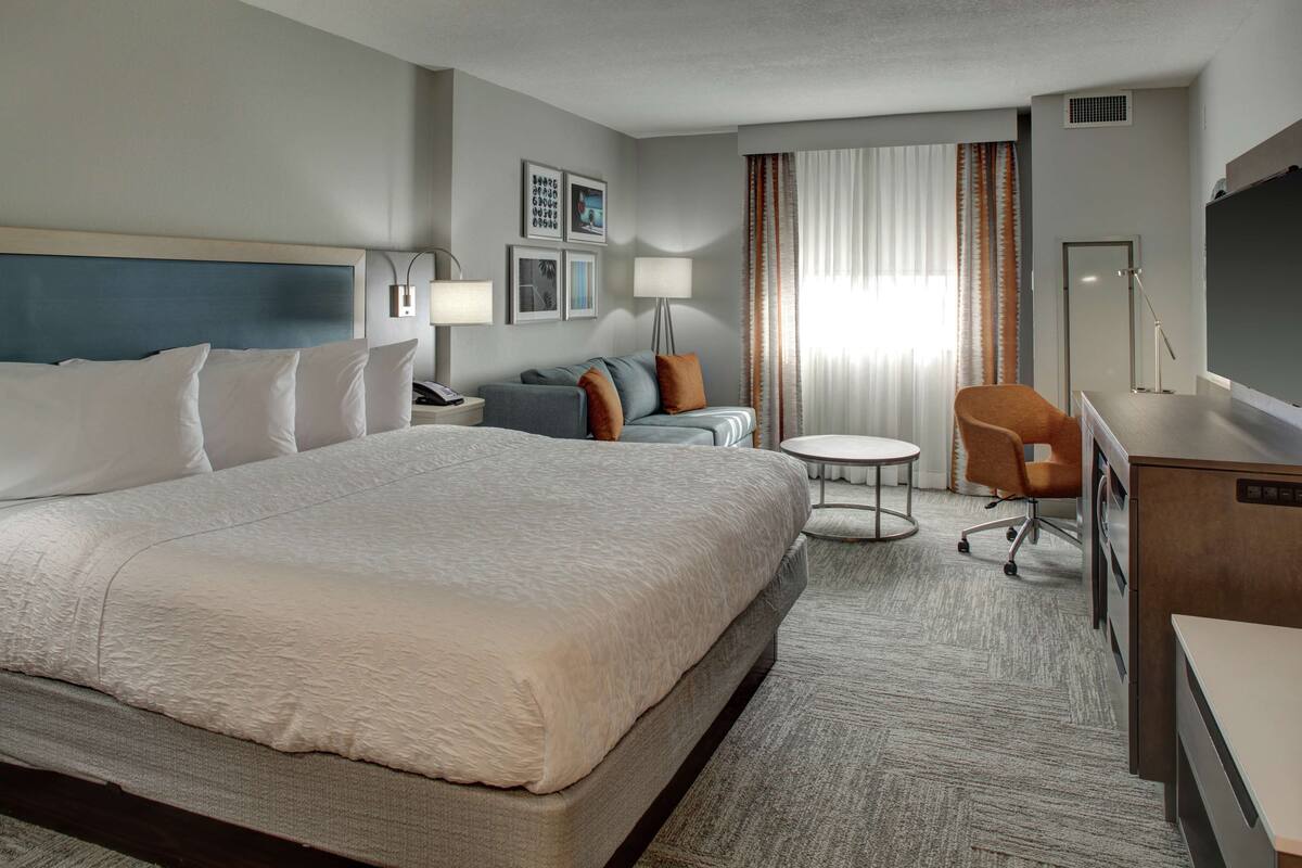 Une chambre d’hôtel avec un grand lit, un bureau, une chaise, une petite table et un canapé.