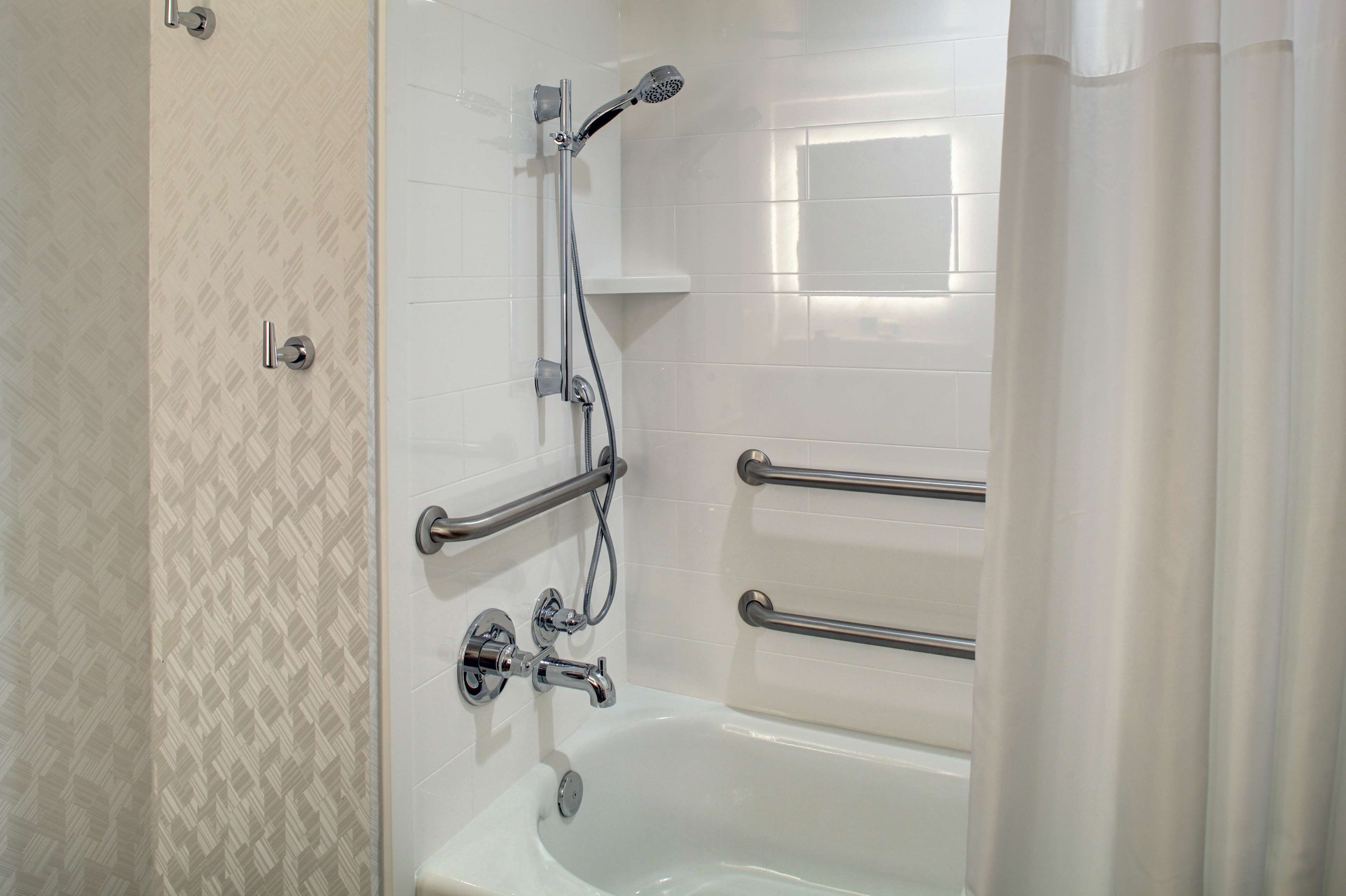 A bathroom with a white bathtub, a shower with a handheld showerhead, and grab bars.