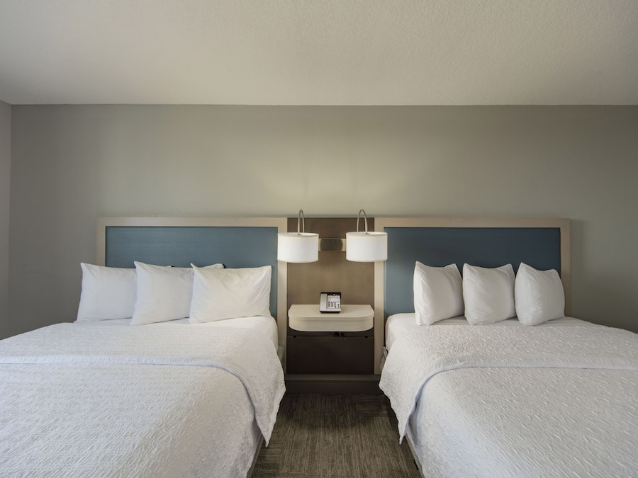 Una habitación de hotel con dos camas, una mesita de noche y una lámpara fijada en la pared.