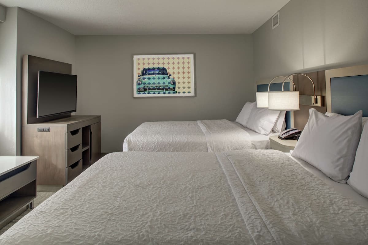 Une chambre d’hôtel avec deux lits, un téléviseur à écran plat, un bureau et un tableau encadré au mur.
