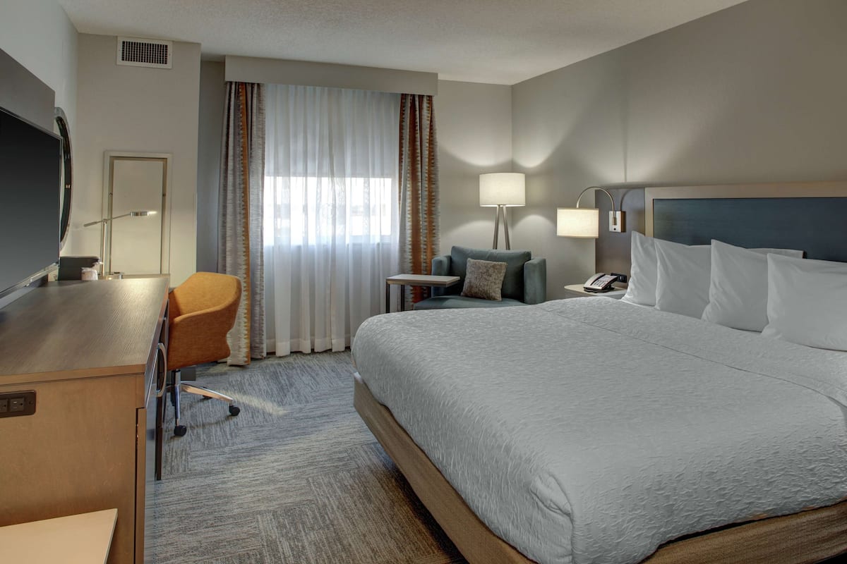 Une chambre d’hôtel avec un grand lit, un bureau avec une chaise, une petite table, une lampe et un téléviseur.