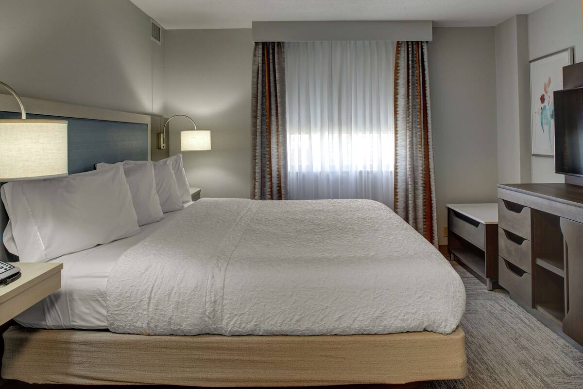 Une chambre d’hôtel avec un grand lit, un bureau avec une lampe, une télévision et une commode.