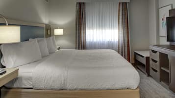A hotel room with a large bed, a desk with a lamp, a TV, and a dresser.