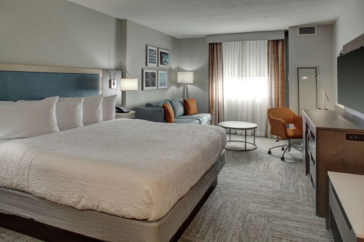 Une chambre d’hôtel avec un grand lit, un bureau, une chaise, une petite table et un canapé.