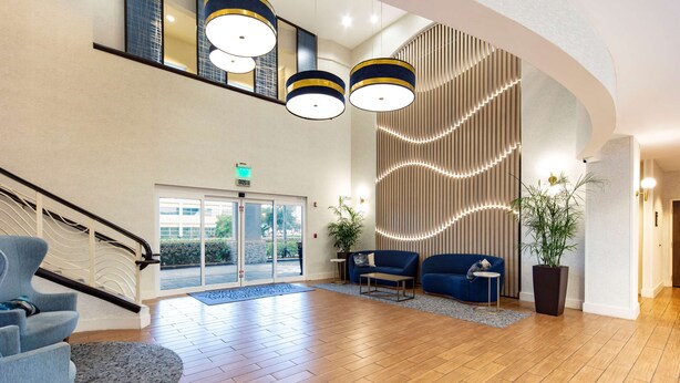 Un amplio vestíbulo con suelo de madera, un sofá azul, una escalera y una pared grande con líneas verticales.