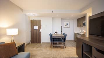 Habitació d'hotel amb sofà, taula de menjador amb cadires, televisió i zona de cuina equipada.