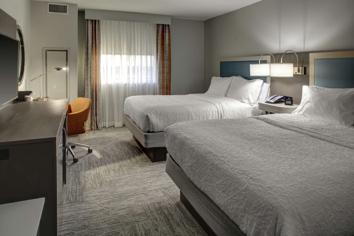 Une chambre d’hôtel avec deux lits, un bureau, une chaise et un téléviseur.
