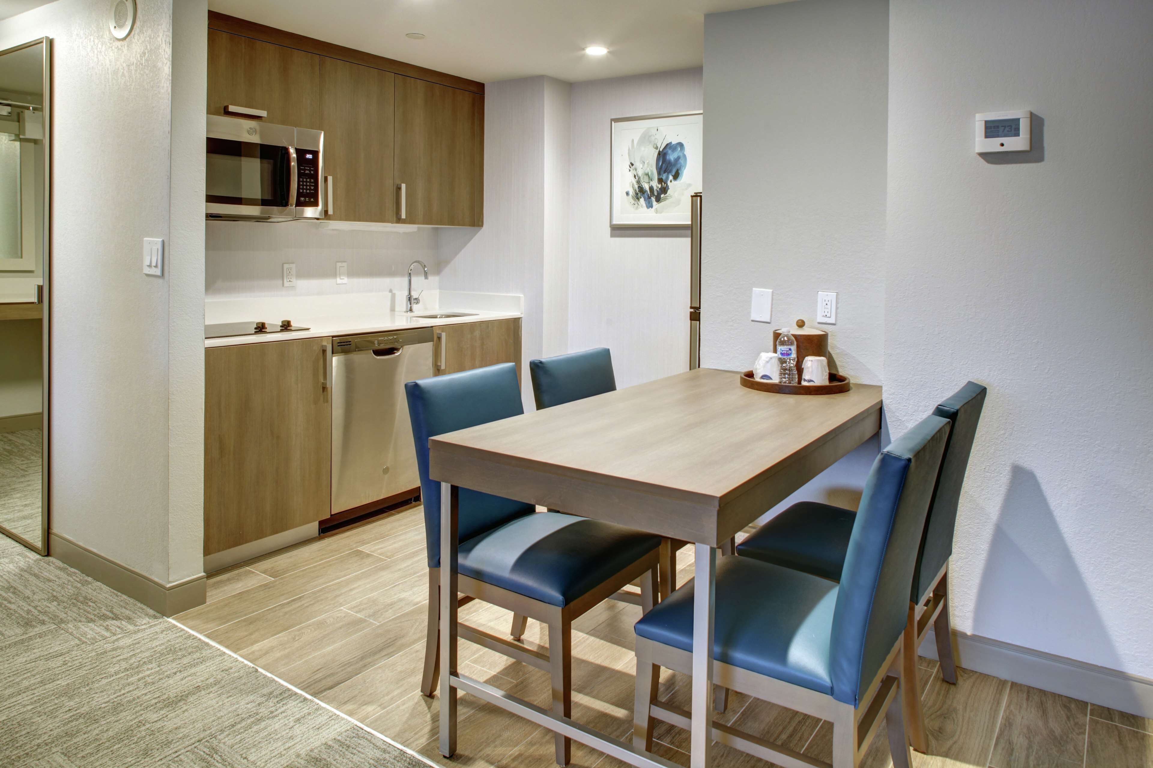 Una cocina moderna con armarios de madera, un microondas y un lavabo. Hay una mesa de comedor con sillas azules.
