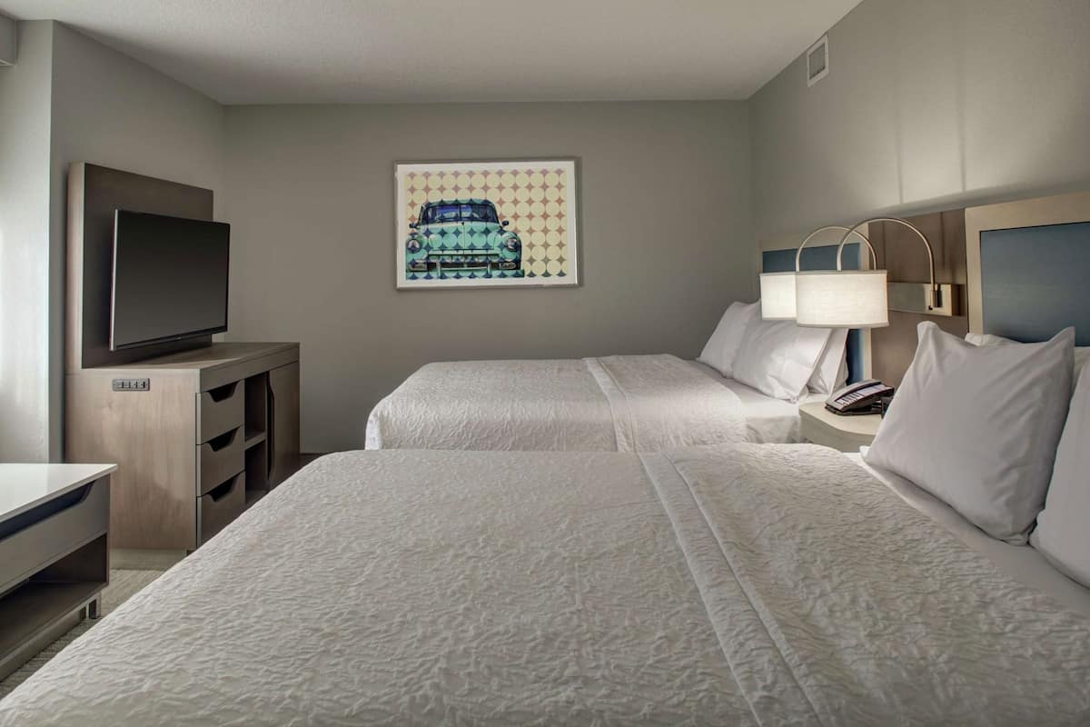 Une chambre d’hôtel avec deux lits, une télévision, un bureau et un tableau au mur.