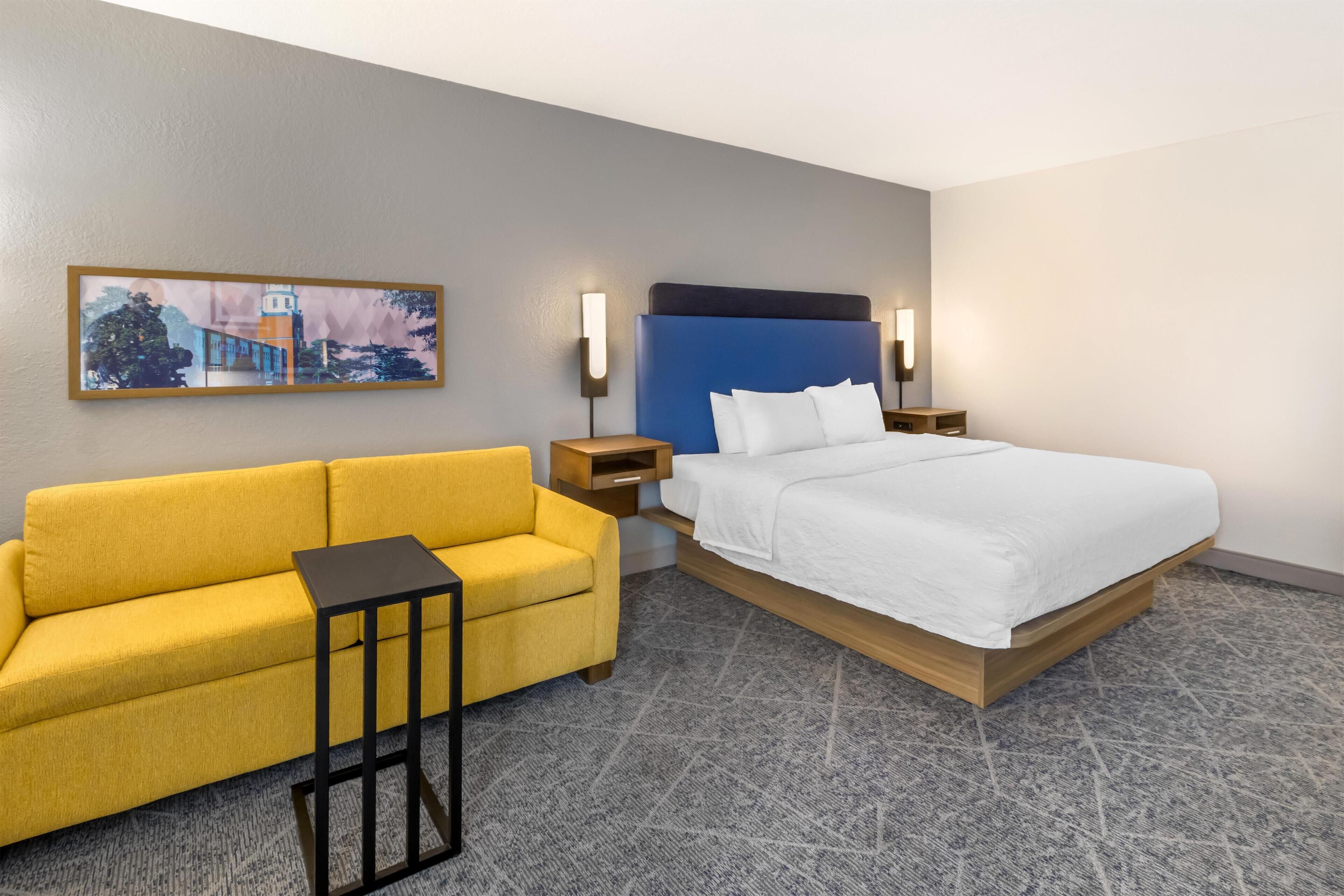 Ein Hotelzimmer mit einem Bett, einer Sitzecke, einem kleinen Tisch, zwei Nachttischen und einer Wandleuchte.