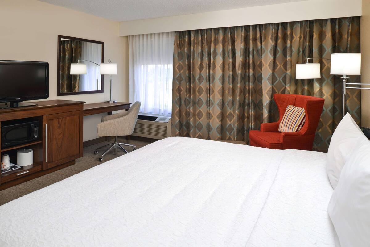 A hotel room with a bed, a desk, a television, a chair, and a large window with curtains.