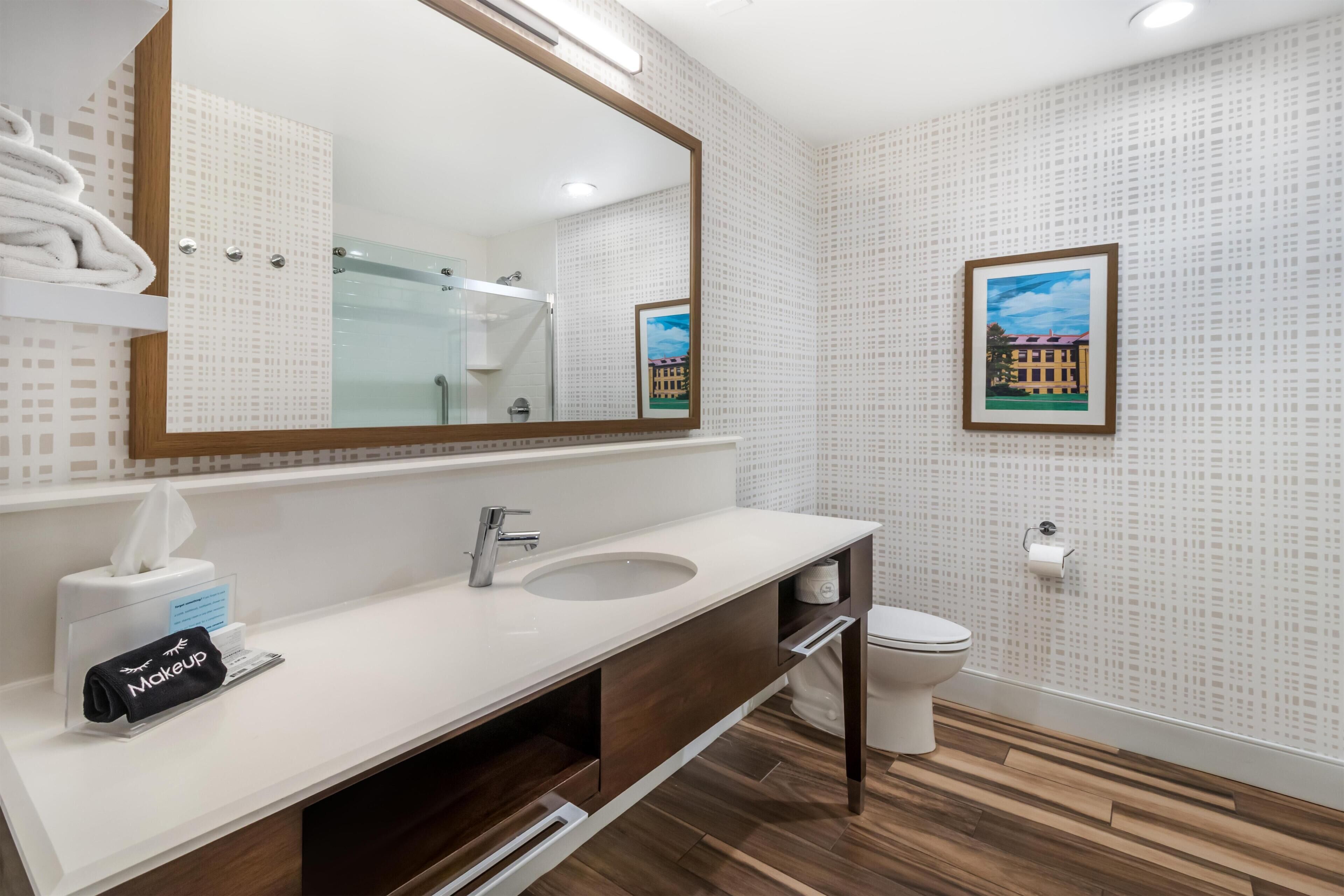 Un baño moderno con un espejo grande, un lavamanos, un inodoro y una ducha.