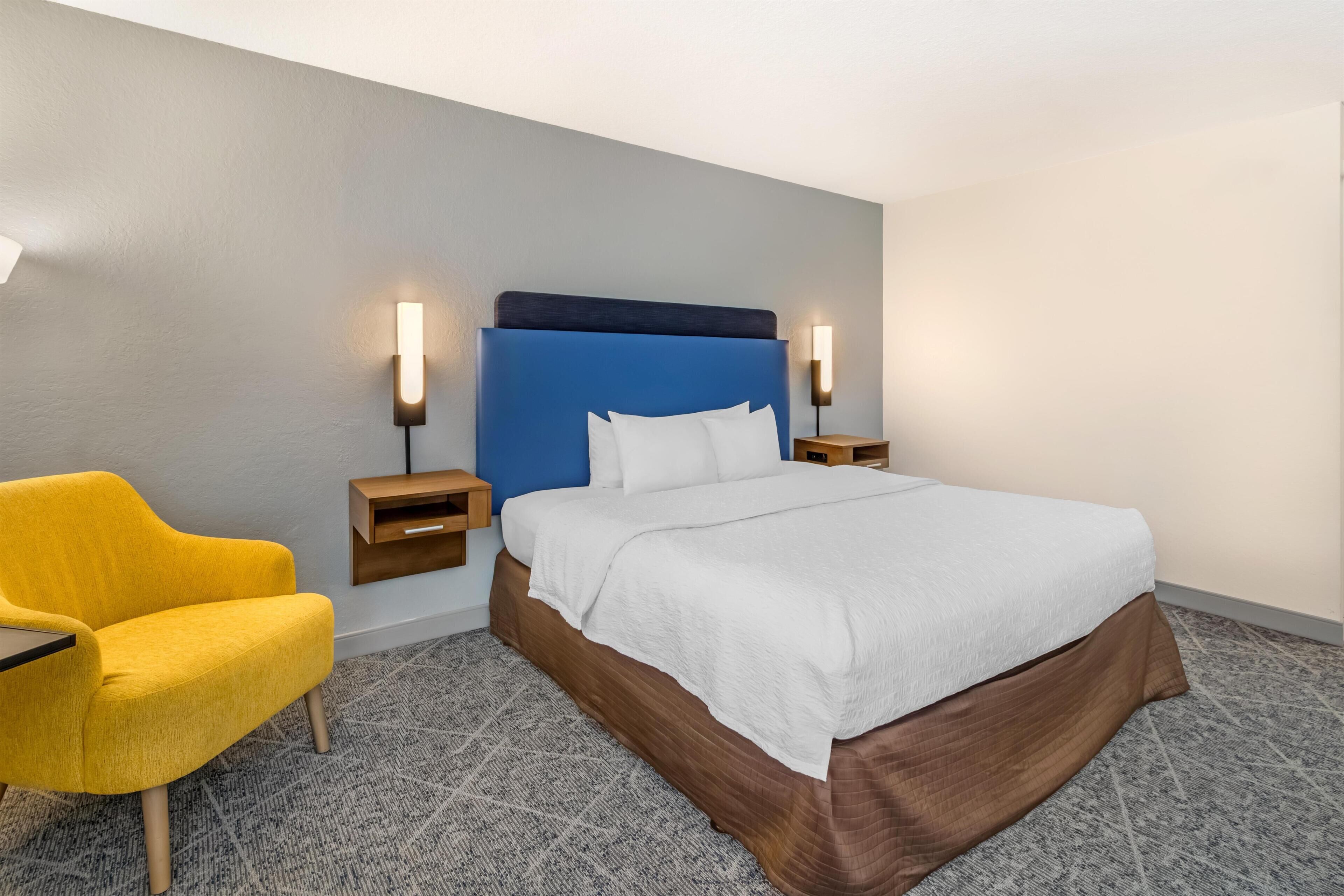 Ein Hotelzimmer mit Bett, Nachttisch, Lampe und Stuhl.