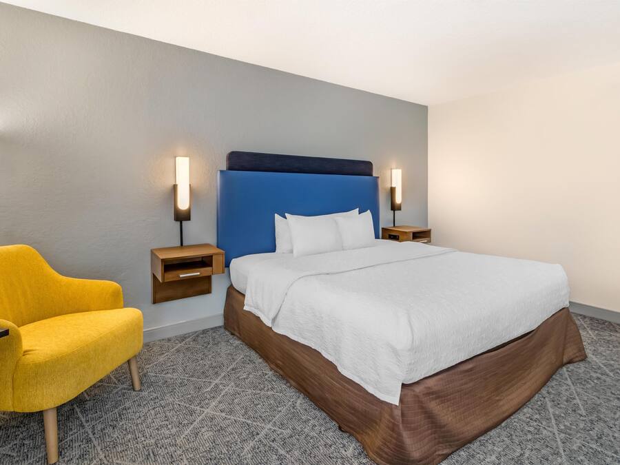 Ein Hotelzimmer mit Bett, Nachttisch, Lampe und Stuhl.