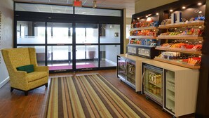 Eine Lobby mit Teppichmuster, einem gelben Sessel, einem Glastür-Eingang und Regalen voller Snacks und Getränke.
