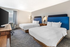 Una habitación de hotel con dos camas, un escritorio, una silla y una mesita de noche.