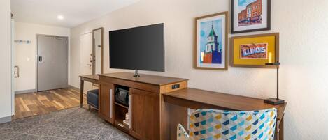 Habitación de hotel con un escritorio de madera, un televisor de pantalla plana, un sillón estampado y cuadros en la pared.