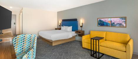 A hotel room with a bed, a sofa, a desk, and a television.
