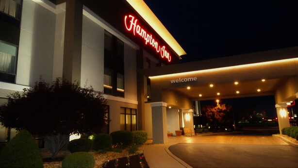 Ein Hotel Eingang mit einem 'Welcome'-Schild und einem 'Hampton Inn'-Schild.