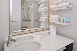 A bathroom with a large mirror, a sink, and shelves with towels and toiletries. - Hampton Inn Carbondale (Carbondale)