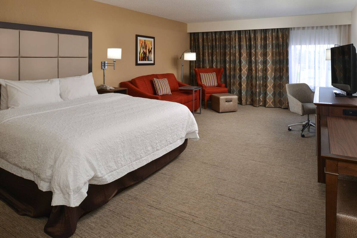 A hotel room with a large bed, a desk with a television, a chair, and a small table.