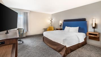 Habitación de hotel con una cama grande, un escritorio con televisión de pantalla plana, una silla y una mesita.