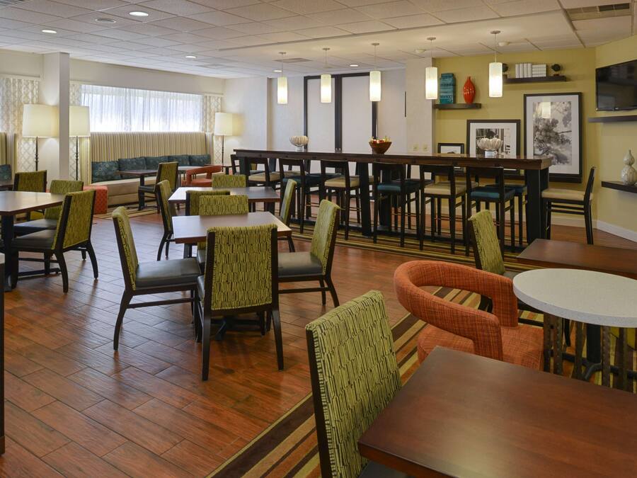 A hotel dining area with multiple tables and chairs, a bar, and a sofa.