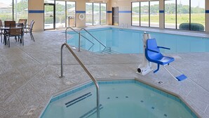 Ein Innenpool mit Rettungsschwimmerstuhl, Liegestühlen am Beckenrand und freiem Blick ins Freie.