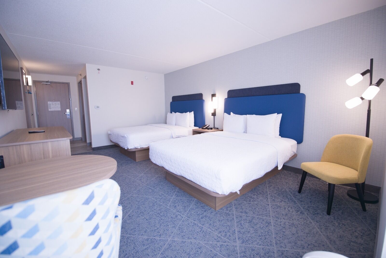 A hotel room with two beds, a desk, a chair, and a bedside table.
