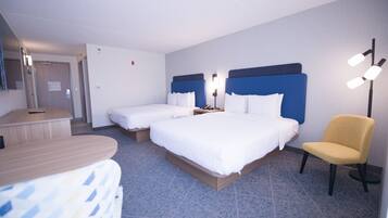 A hotel room with two beds, a desk, a chair, and a bedside table.