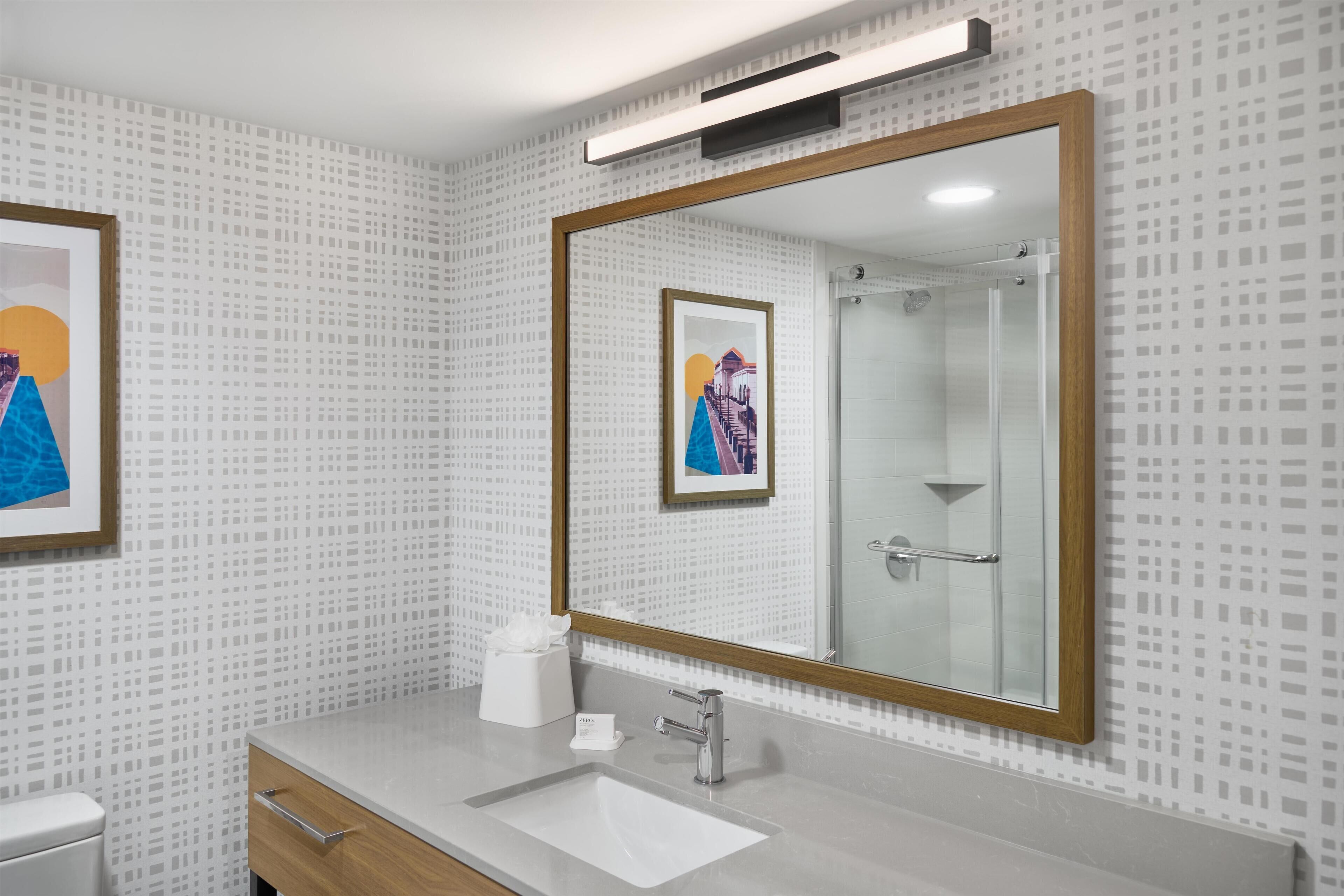 Un baño moderno con un espejo grande, un lavamanos y una ducha.