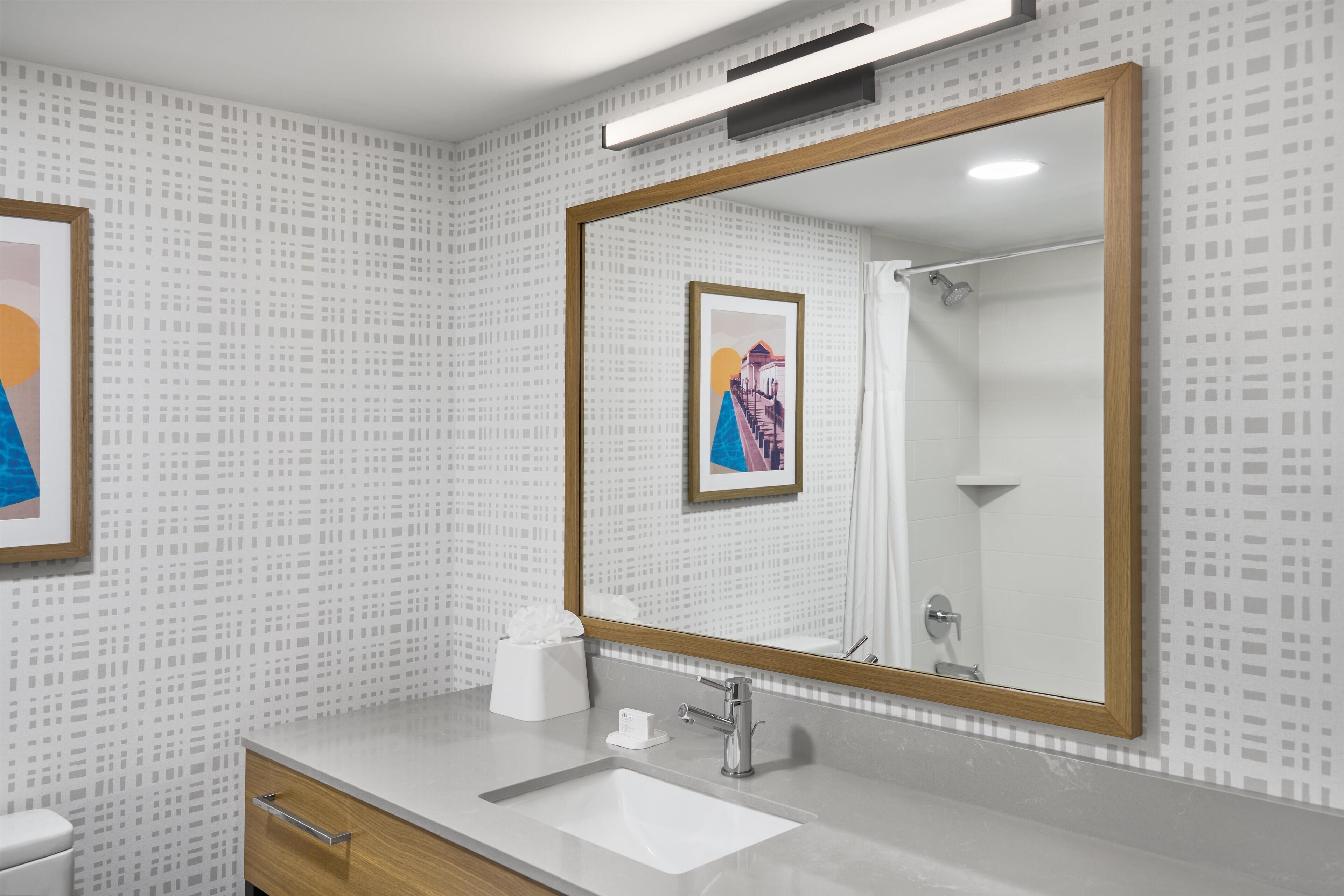 A modern bathroom with a large mirror, a white sink, and a wooden cabinet.