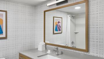 A modern bathroom with a large mirror, a white sink, and a wooden cabinet.