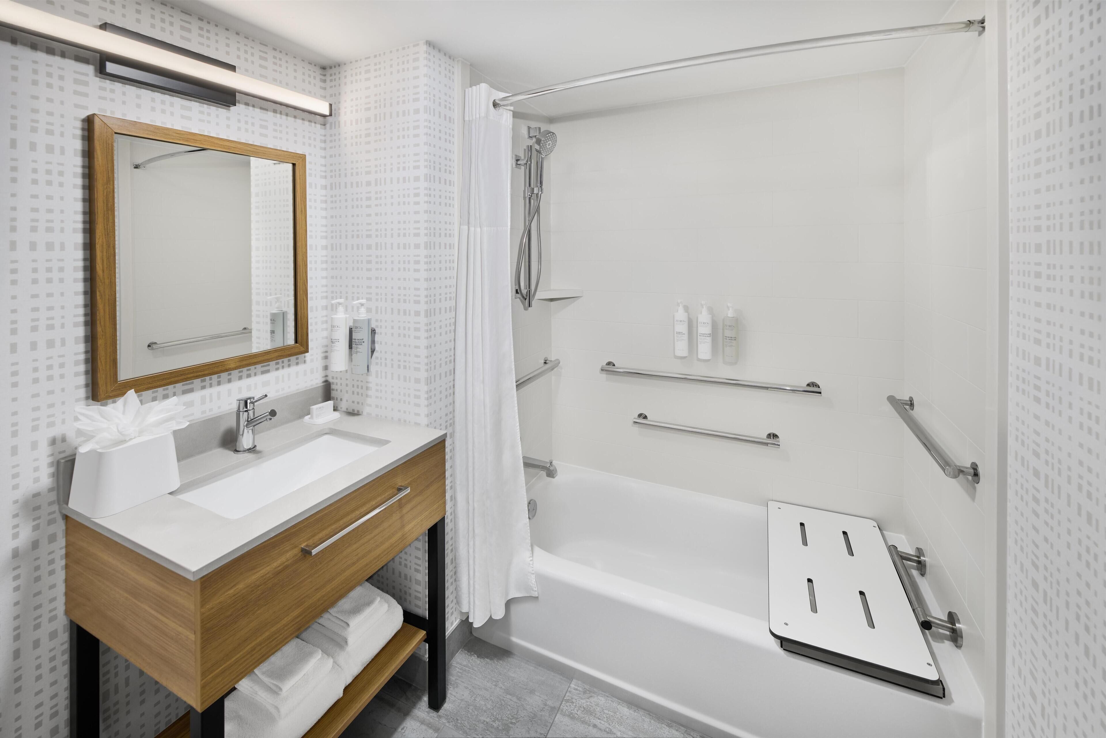 A modern bathroom with a wooden vanity, a large mirror, a bathtub, and a shower area.