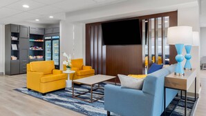 Un hall d’hôtel moderne avec un canapé, des fauteuils, une table basse, un téléviseur et un mini-bar.