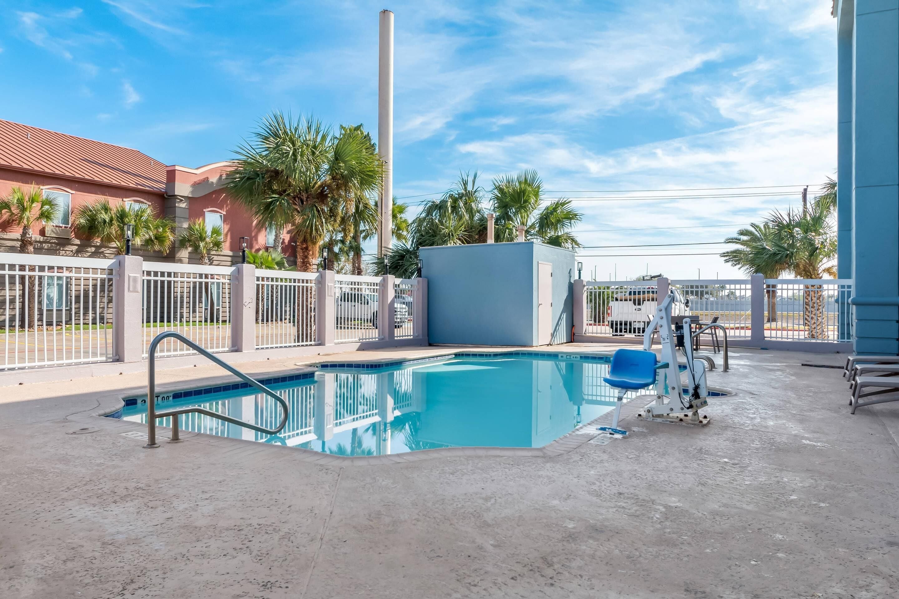 A swimming pool with a metal ladder, surrounded by a white fence and palm trees.