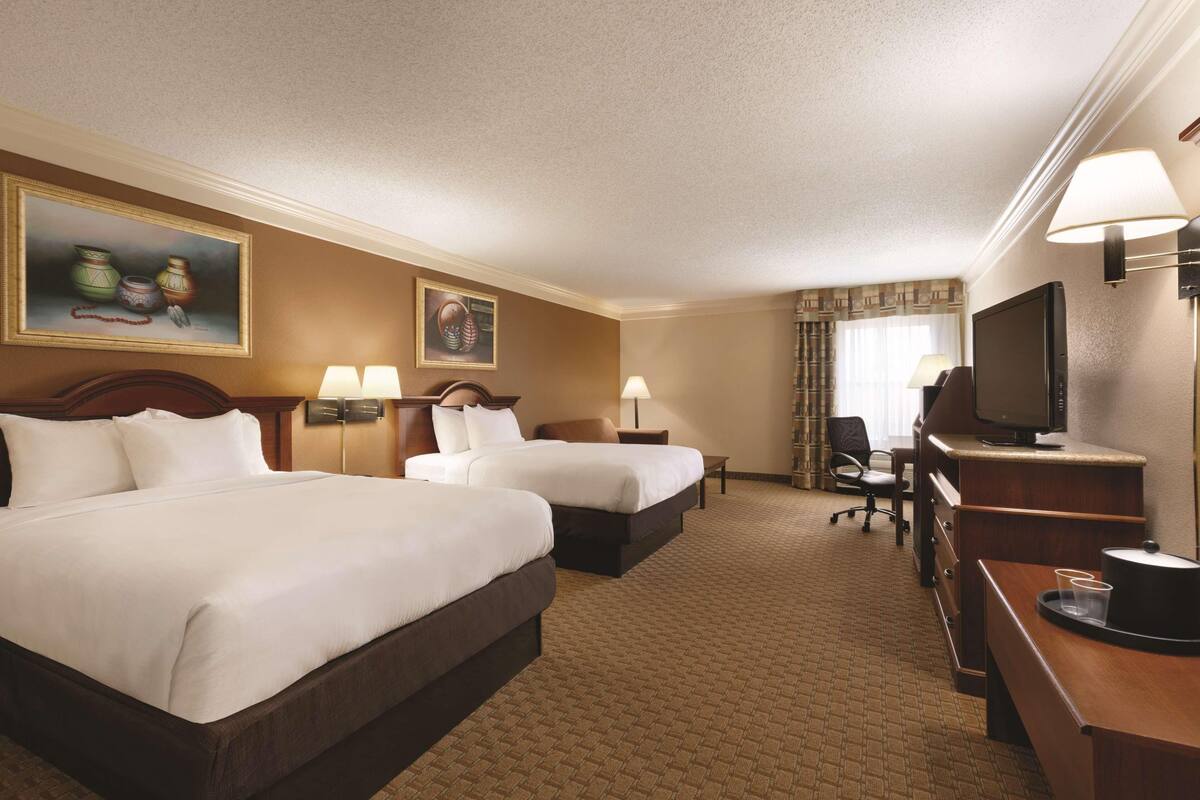 A hotel room with two beds, a desk, a television, and artwork on the walls.