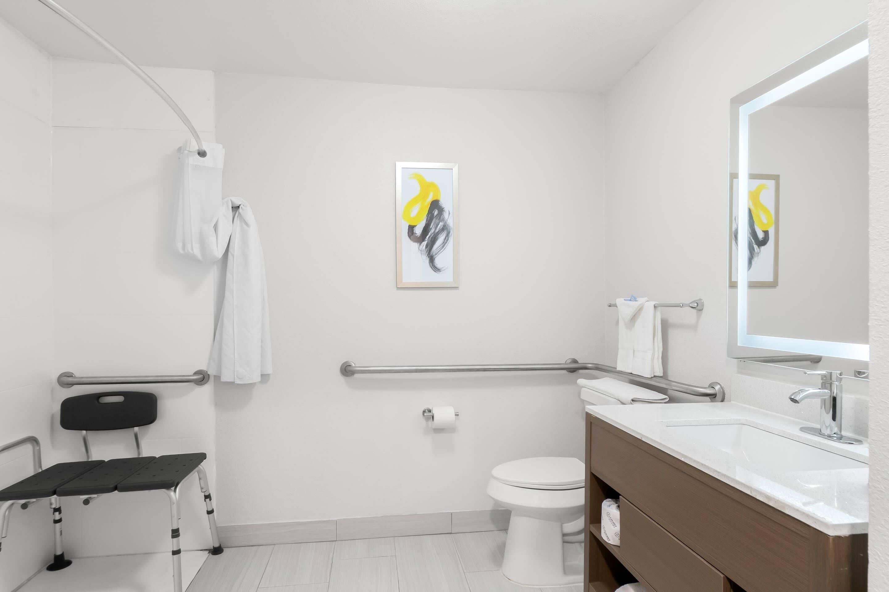 Een moderne badkamer met douche, toilet en wastafel. Er staat een rolstoel en er is een handgreep.