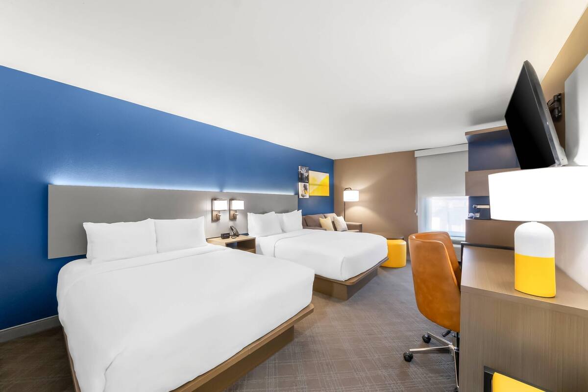 A hotel room with two beds, a desk, a chair, and a TV.